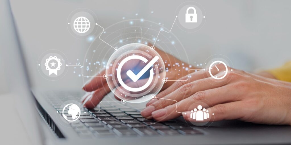 Pessoa digitando em um laptop com ícones tecnológicos flutuando sobre o teclado, incluindo um grande ícone de verificação no centro e símbolos de segurança e conectividade ao redor.