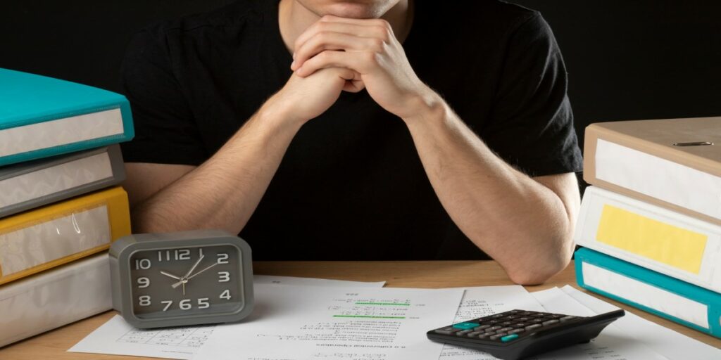 Imagem de homem ao lado de documentos com calculadora e relógio em mesa 